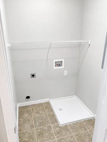 Dedicated utility space featuring tile flooring, a built-in wire shelf, appliance hookups, and a recessed drain pan
