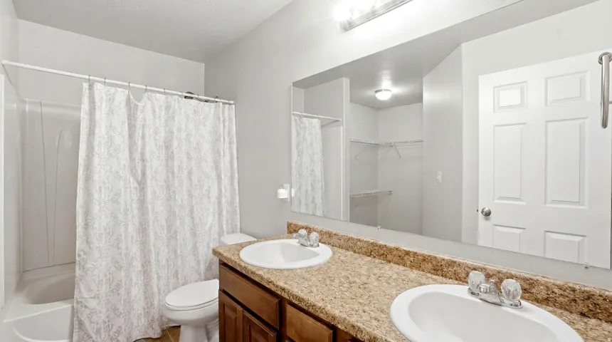 Bathroom featuring a dual vanity with a speckled countertop, undermount sinks, and a full-width mirror