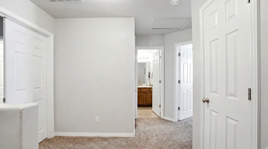 Carpeted hallway with white interior doors, light-toned walls, and white trim