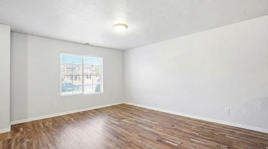 Spacious room featuring wood-finish flooring, white baseboards, and a large window with blinds