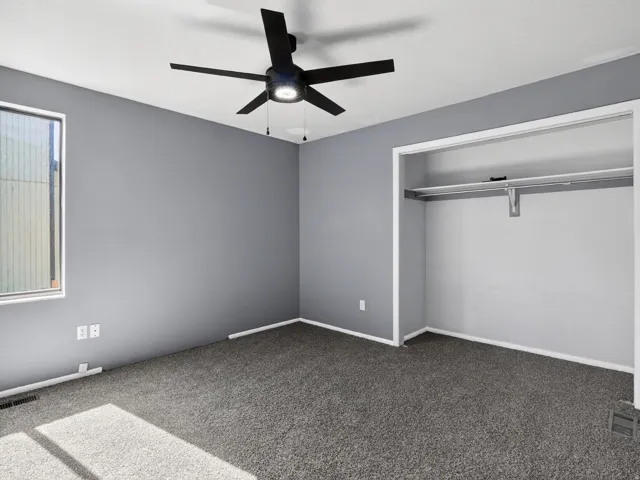 Room featuring gray wall paint, gray carpeting, a window with white trim, and a built-in closet with shelving and hanging rod