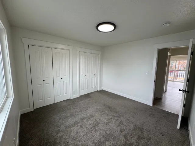 Spacious room featuring neutral carpeting, two sets of bi-fold closet doors, a contemporary flush-mount ceiling light, and white trim throughout