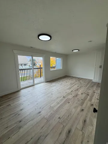 Spacious room with wood-finish flooring, recessed lighting, and a glass sliding door leading to a balcony