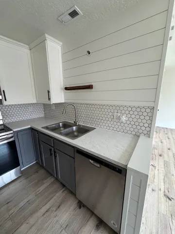 Kitchen featuring two-tone cabinetry with white upper and gray lower cabinets, light-colored countertops, a double basin stainless steel sink, and a stainless steel dishwasher
