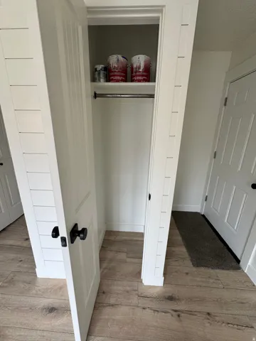 Integrated closet with a metal hanging rod and an upper shelf, complemented by wood-finish flooring and white paneled doors with black hardware