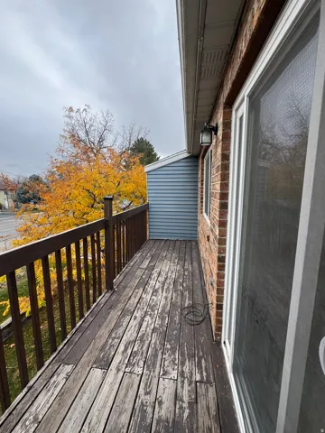 Exterior balcony featuring a brick facade, wood railing, and vinyl siding