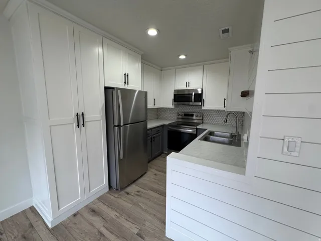 Kitchen featuring white shaker cabinetry, stainless steel appliances, a honeycomb tile backsplash, wood-finish flooring, and shiplap paneling