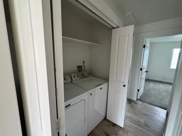 Dedicated laundry area featuring a white top-load washer and dryer set, an overhead storage shelf, and plank-style flooring