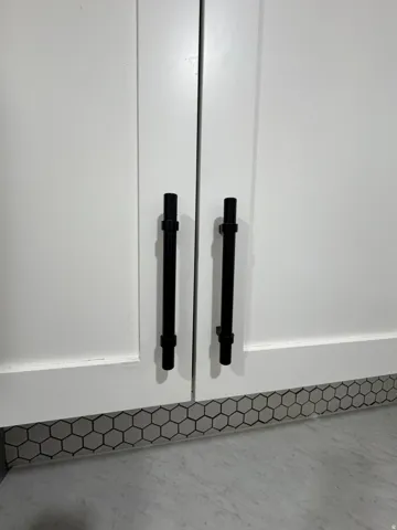 White cabinetry with matte black bar pulls and a hexagonal tile accent border