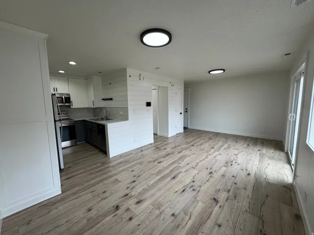 Open-concept living area featuring wood-finish flooring, a contemporary kitchen, stainless steel appliances, white cabinetry, and shiplap accents