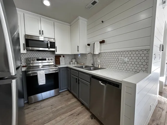 Contemporary kitchen featuring stainless steel appliances, two-tone cabinetry with white upper and gray lower cabinets, hexagon tile backsplash, wood-finish flooring, and white shiplap wall paneling