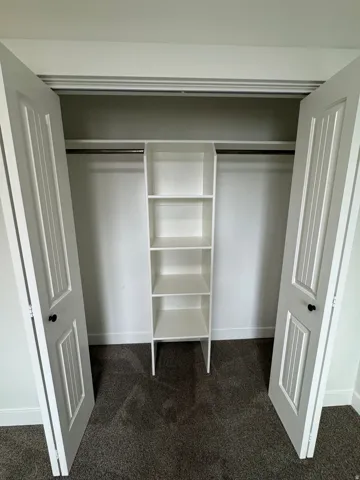 Closet featuring dual bifold doors, built-in shelving, hanging rods, and dark gray carpeting