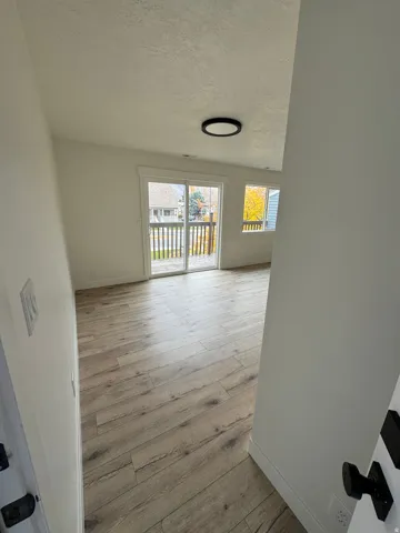 Spacious living area featuring wood-finish flooring, white walls, and a contemporary flush-mount ceiling light