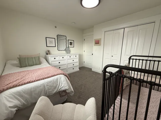 Carpeted room featuring a white paneled closet, a white dresser with black hardware, and a single paneled door with black hardware