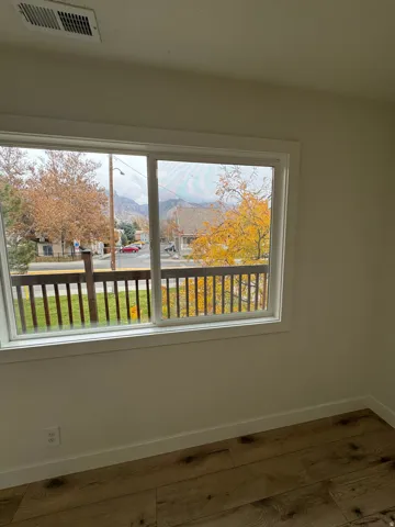Large window with white trim, wood-finish flooring, white baseboards, and a ceiling vent