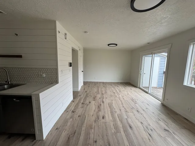 Open-concept living area featuring wood-finish flooring, white shiplap accent wall, white hexagonal tile backsplash, a sliding glass door, and flush-mount lighting fixtures