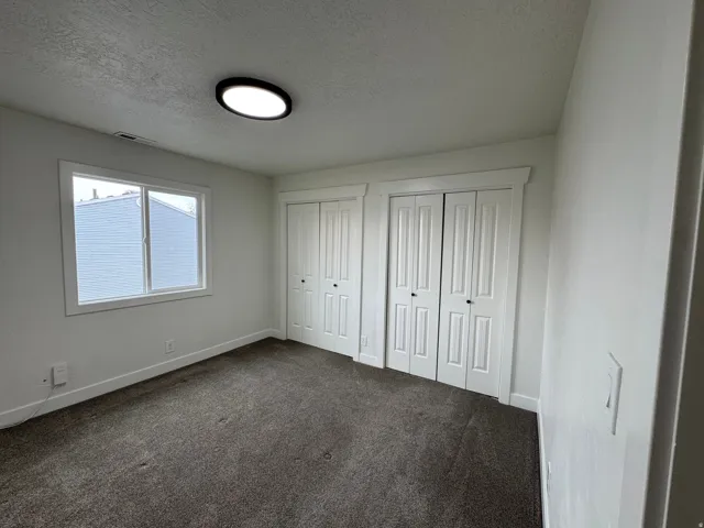 Bedroom featuring neutral carpeting, a dual-pane window with white trim, two white bi-fold closet doors, and a flush-mount ceiling light fixture