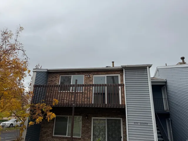 Exterior facade featuring brick and horizontal siding, an upper-level balcony with wood railing, and ground-level windows