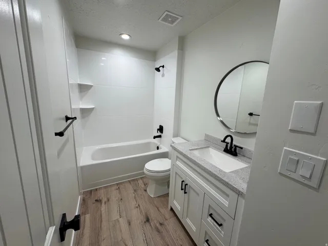 Bathroom featuring a white vanity with a speckled countertop, a round mirror, and a white bathtub with black fixtures