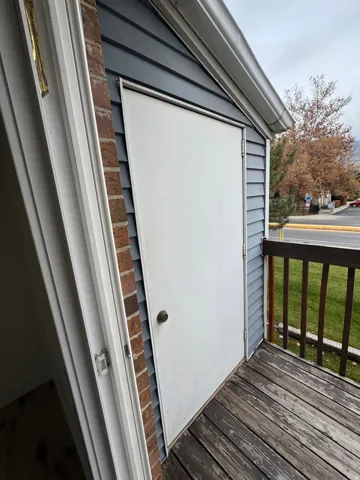 Exterior storage door with a round knob handle, wood-finish decking, and dark gray horizontal siding
