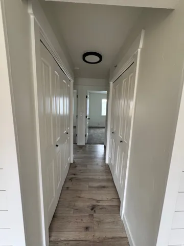 Hallway featuring wood-finish flooring, white paneled doors with black hardware, and a modern flush-mount ceiling light fixture