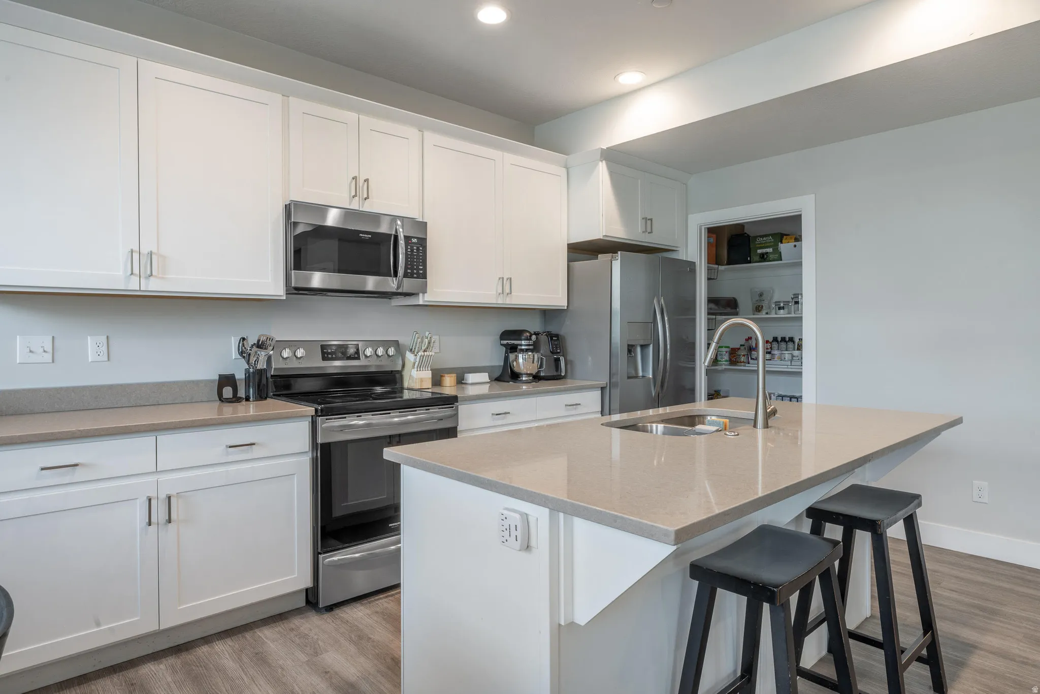 Modern kitchen featuring white cabinetry, stainless steel appliances, a center island with an undermount sink, light-toned countertops, and wood-finish flooring