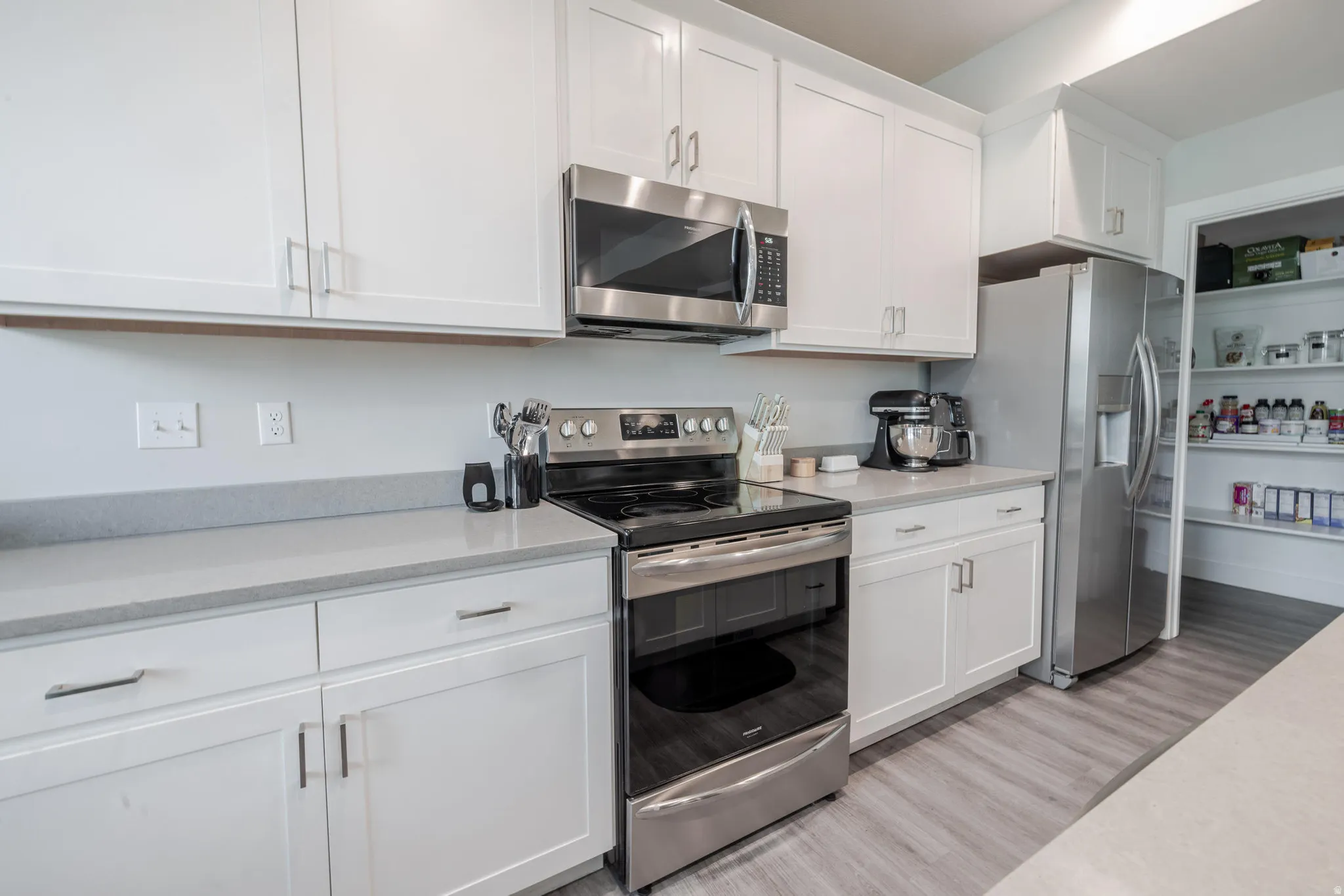 Kitchen featuring white cabinetry with brushed nickel hardware, light gray countertops, stainless steel appliances, and wood-finish flooring