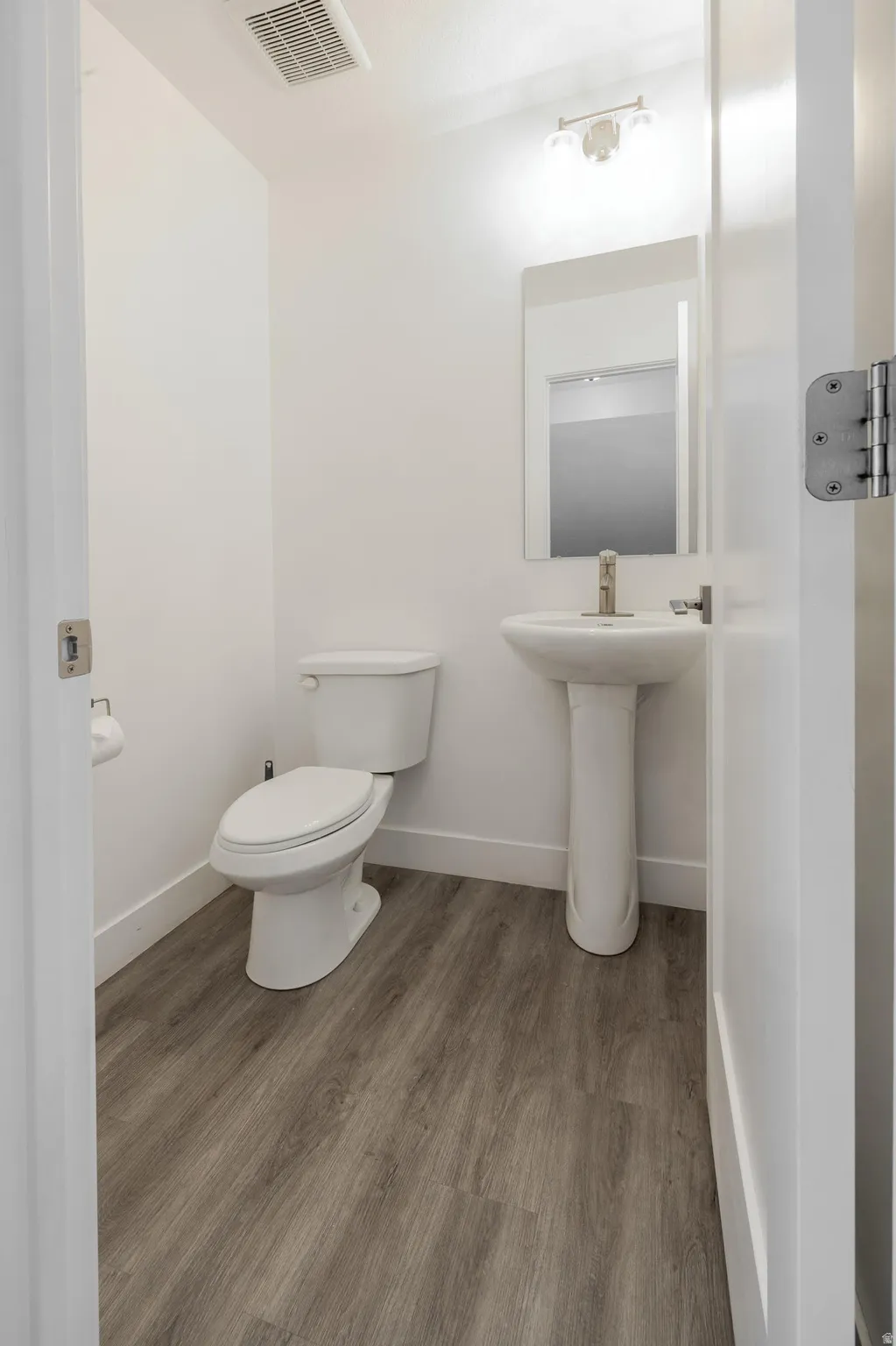 Bathroom featuring a white pedestal sink with a brushed nickel faucet, an oval mirror, and a white toilet