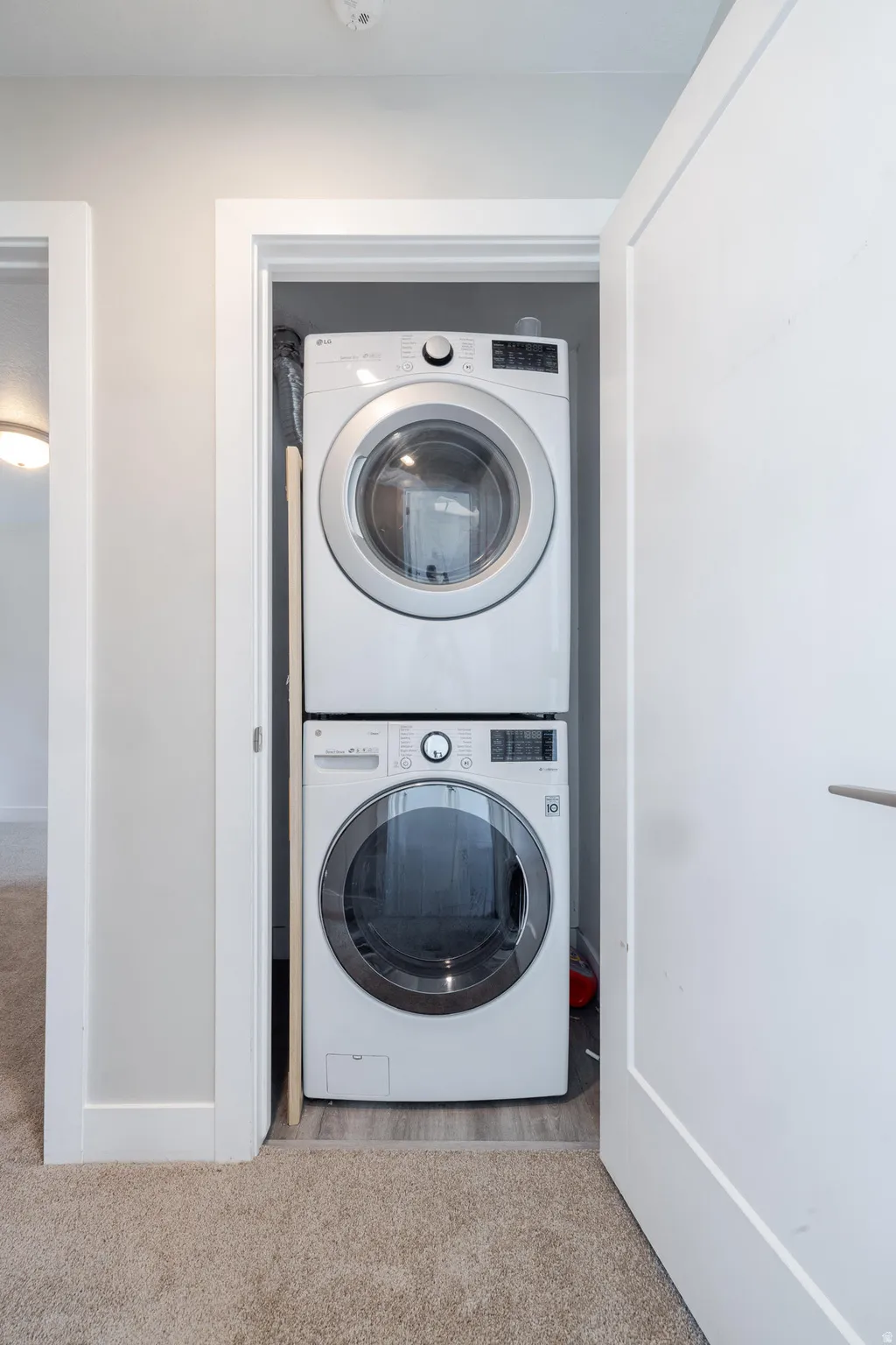 Built-in laundry closet featuring a stacked white washer and dryer unit, wood-finish flooring, and a white interior door