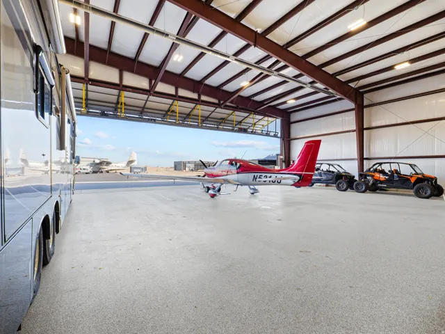 Spacious hangar featuring a high ceiling with exposed steel beams, industrial lighting, and a wide-span overhead door