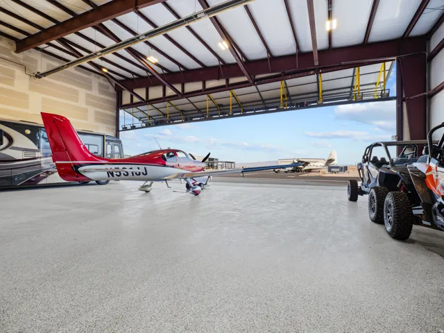 Aircraft hangar featuring a large bi-fold door, exposed structural steel beams, and a light-colored epoxy floor