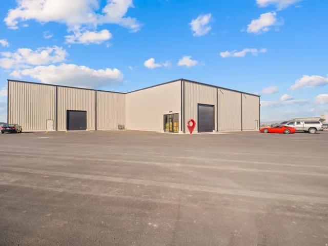 Commercial building featuring corrugated metal siding, black trim, multiple large roll-up doors, and an expansive paved lot