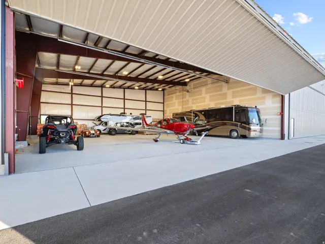 Spacious hangar featuring a large bi-fold door, industrial lighting, exposed structural beams, and a concrete floor
