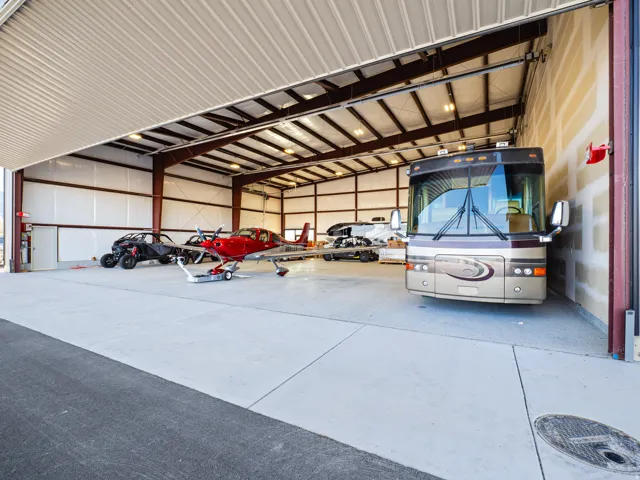 Spacious hangar featuring a large roll-up door, exposed steel beam construction, concrete flooring, and ample overhead lighting