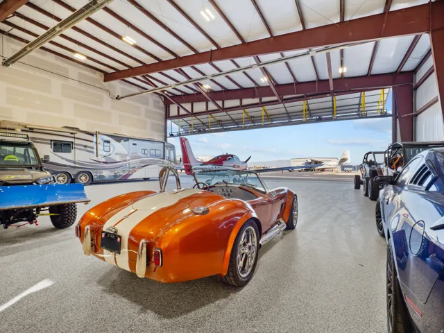 Spacious hangar featuring an epoxy floor, steel beam construction, overhead lighting, and a large accordion-style hangar door
