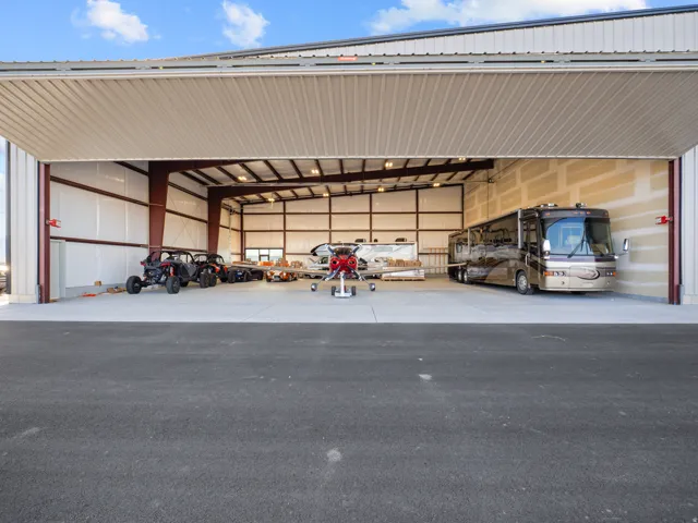 Expansive hangar space featuring a wide bi-fold door, exposed structural steel beams, white metal paneling, concrete flooring, and ample overhead lighting