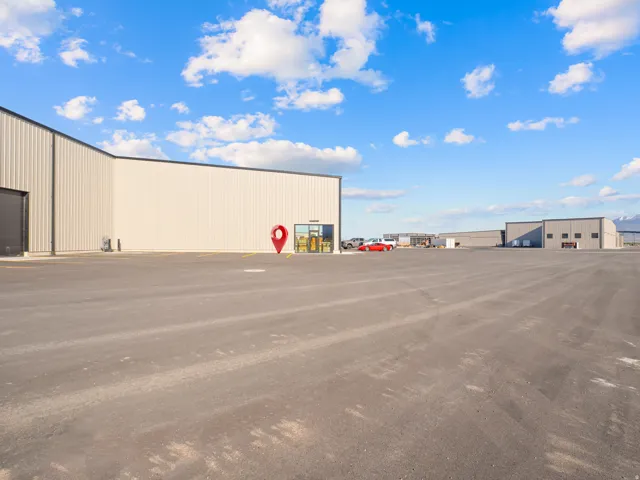 Expansive asphalt lot with a modern industrial building featuring metal siding, a large roll-up door, and a glass-paneled entrance
