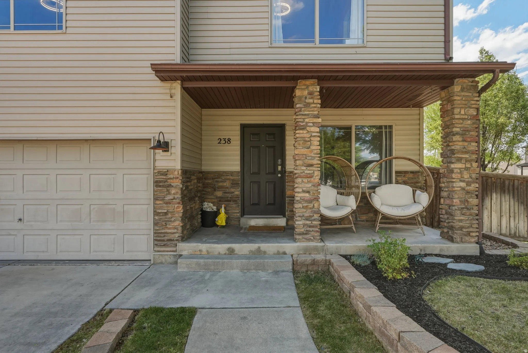Front entry featuring a covered porch with stone-clad columns, horizontal siding, and a paneled garage door
