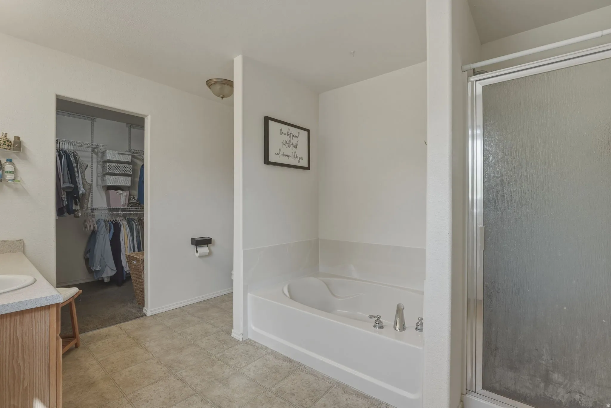 Bathroom featuring a built-in tub, a glass-enclosed shower, wood-finish vanity with an integrated sink, and an adjacent walk-in closet with wire shelving