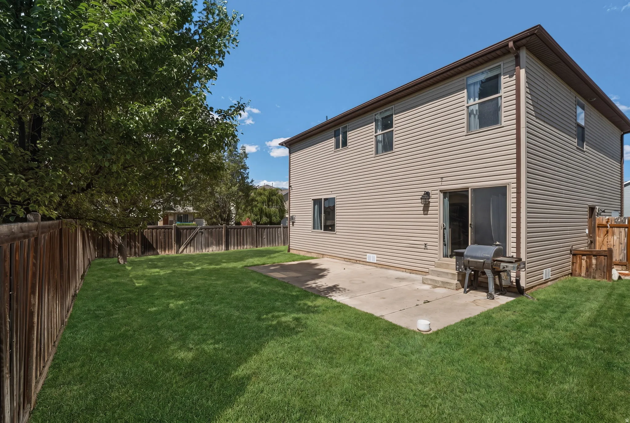 Expansive grassy yard with a privacy fence and mature trees