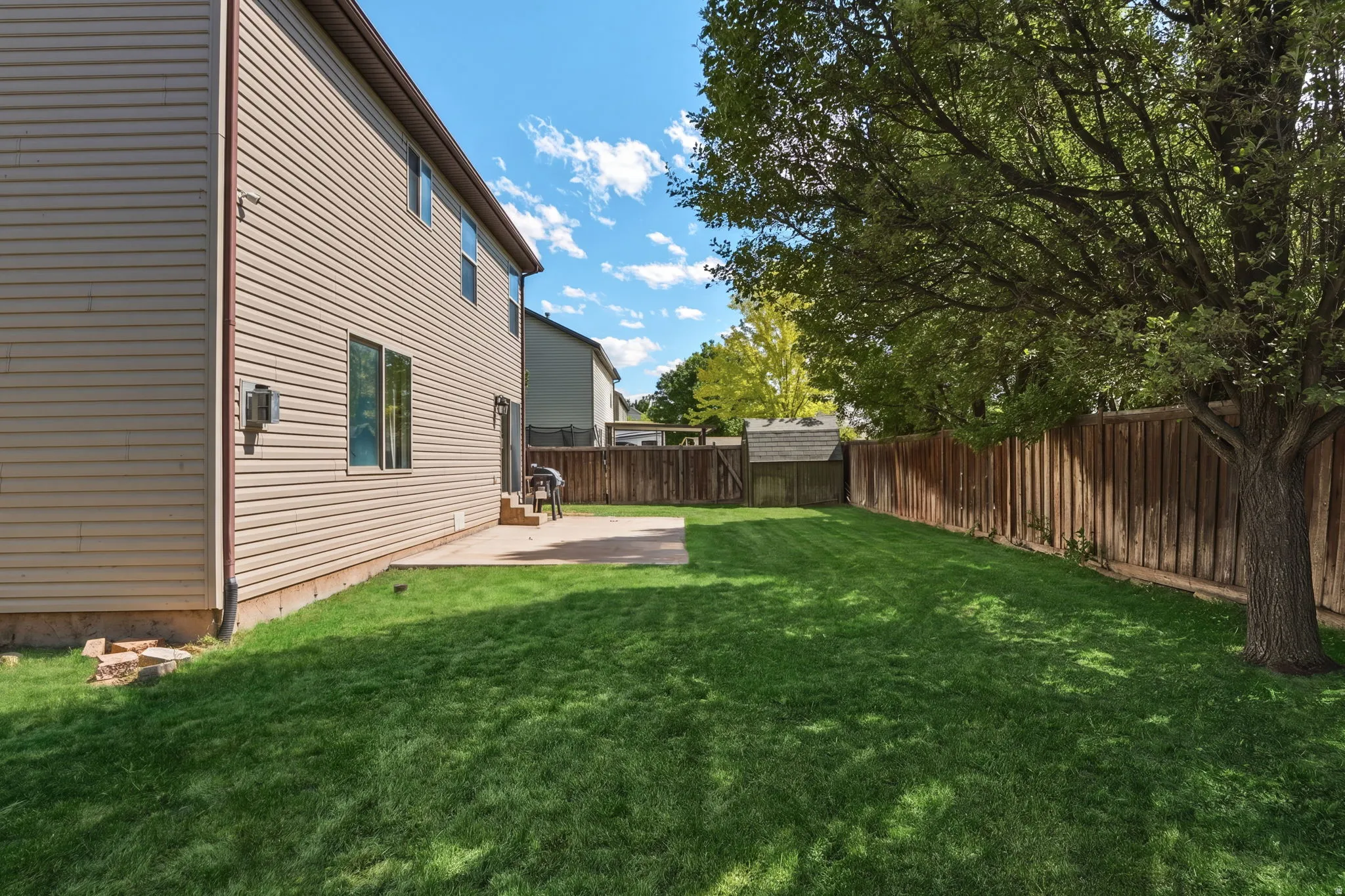 Expansive backyard featuring a manicured lawn, a large concrete patio, and a mature shade tree