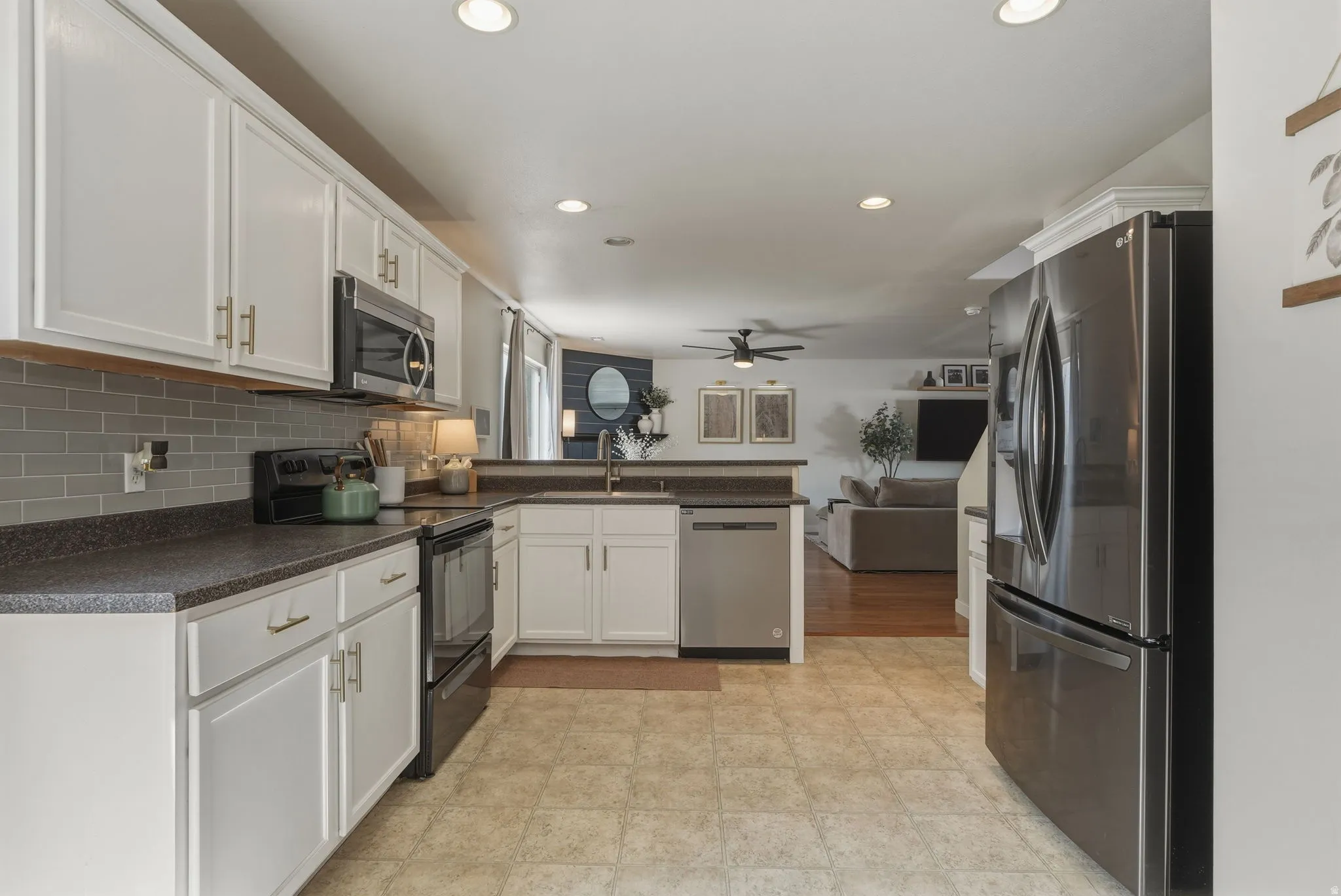 Modern kitchen featuring white cabinetry with gold-tone hardware, dark countertops, a gray subway tile backsplash, and stainless steel appliances