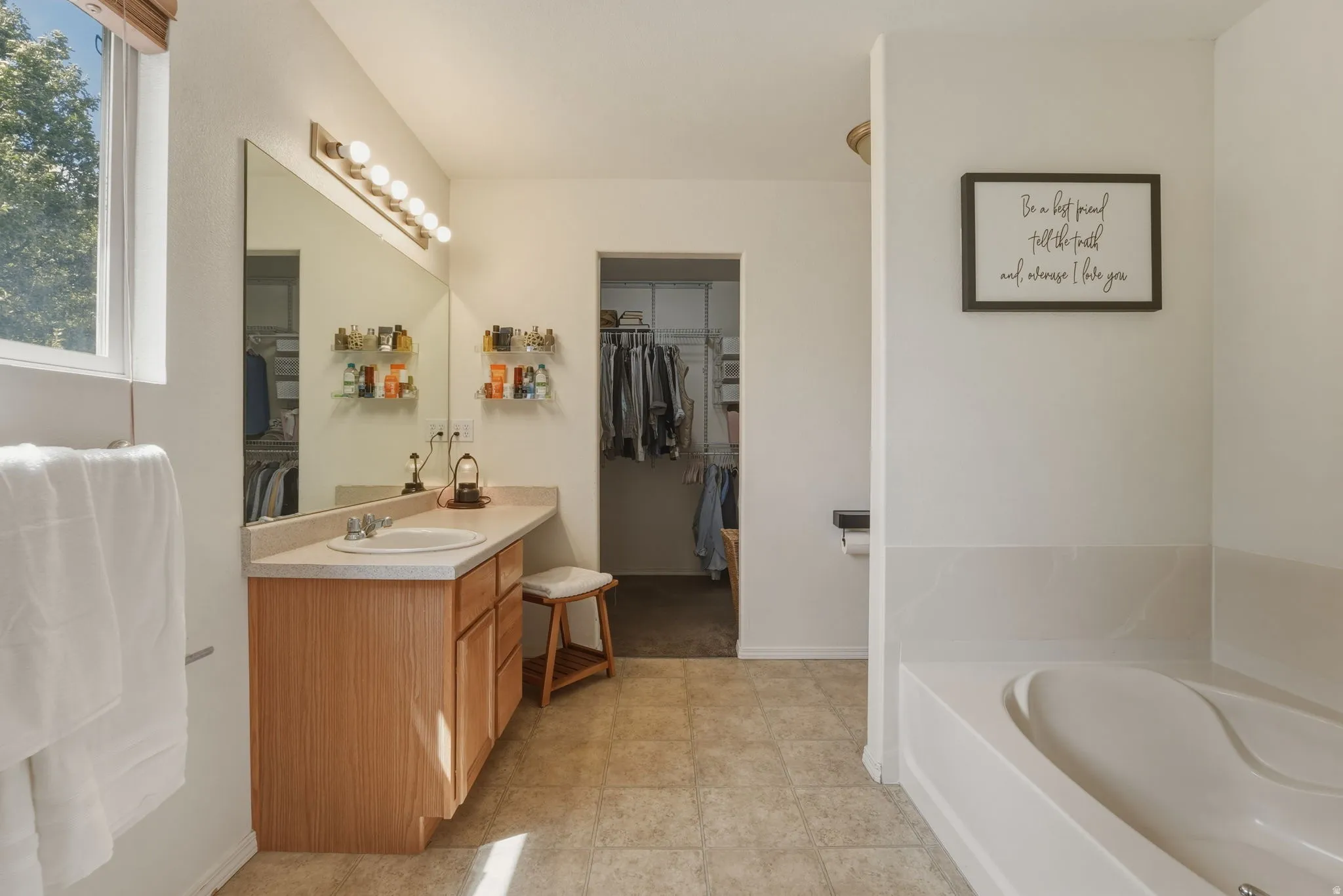 Spacious bathroom featuring a light wood-finish vanity with an integrated sink, a large wall-mounted mirror, and overhead lighting