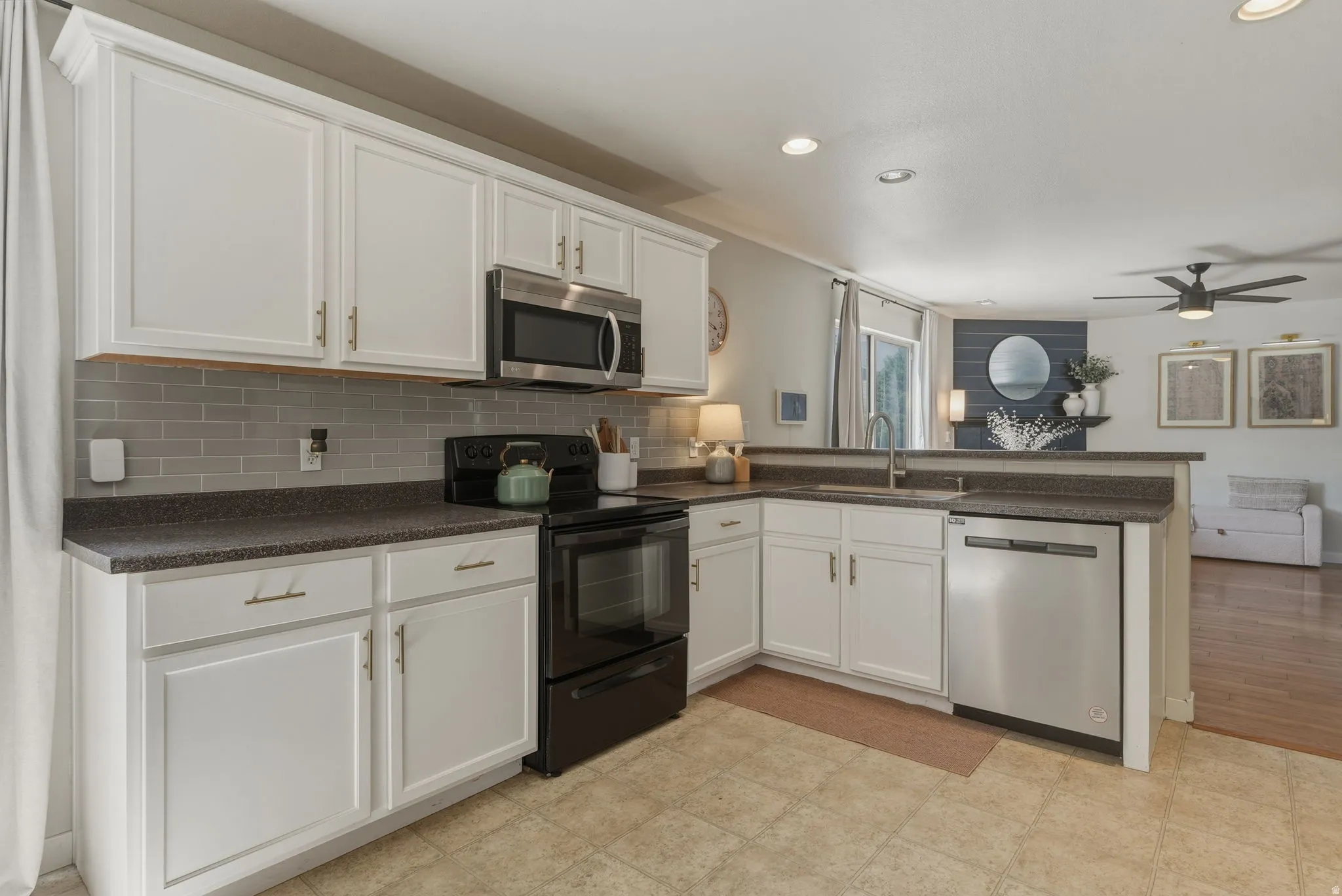 Kitchen featuring white cabinetry, grey subway tile backsplash, dark countertops, and stainless steel dishwasher