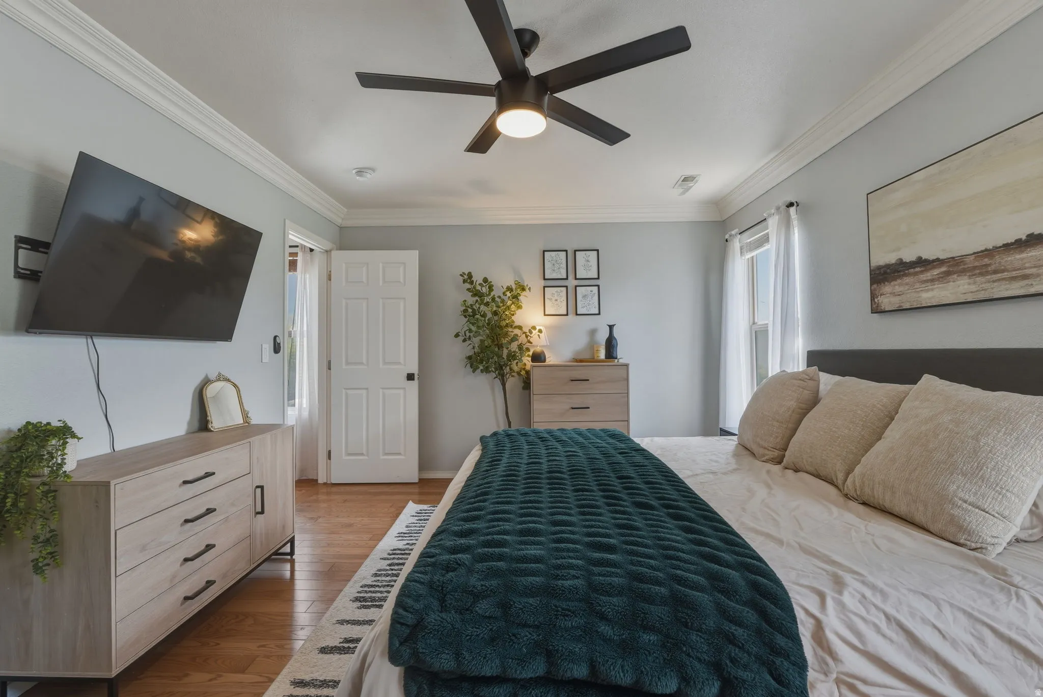 Hardwood-finish flooring throughout, featuring crown molding, a ceiling fan with integrated lighting, and a white paneled door
