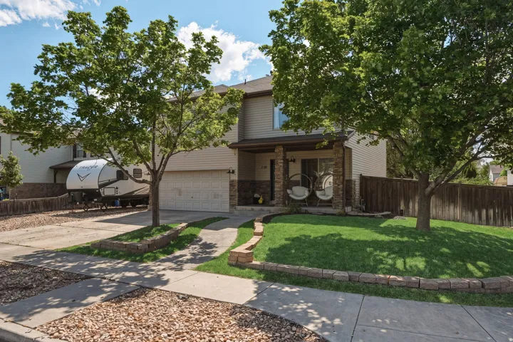 Two-story residence featuring a two-car garage, stone column accents, covered front porch, and mature landscaping