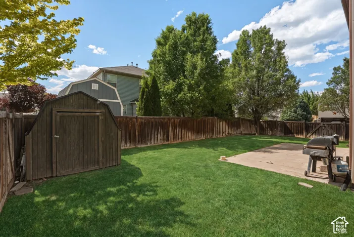 Expansive backyard featuring a lush lawn, mature trees, a wooden privacy fence, a concrete patio, and a storage shed