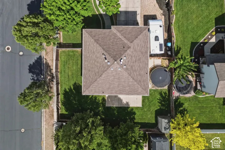 Pitched shingle roof with multiple vents and surrounding green lawns, bordered by mature trees and a paved street