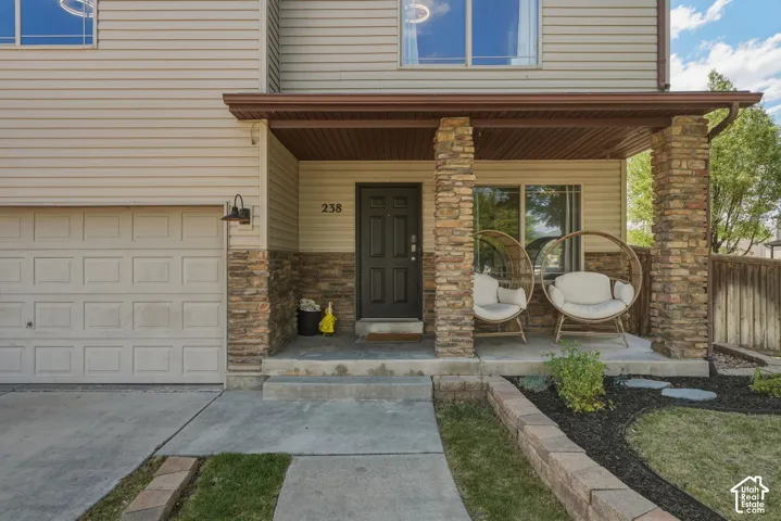 Front entry featuring a covered porch with stone-clad columns, horizontal siding, and a paneled garage door
