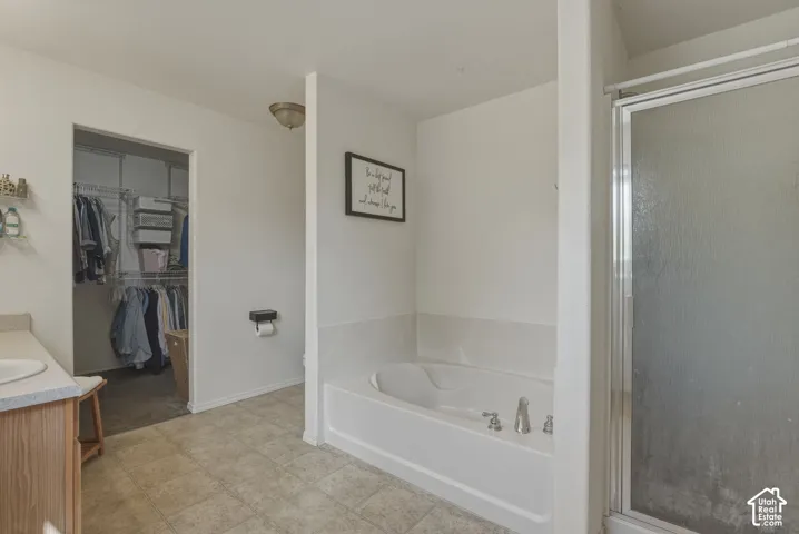 Bathroom featuring a built-in tub, a glass-enclosed shower, wood-finish vanity with an integrated sink, and an adjacent walk-in closet with wire shelving